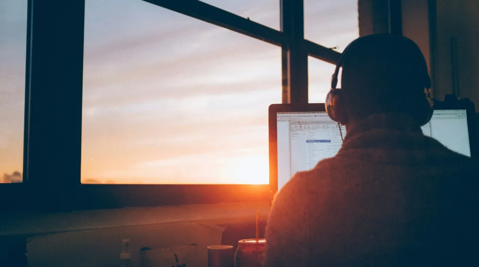 Person working at a computer with headphones against a sunset backdrop.